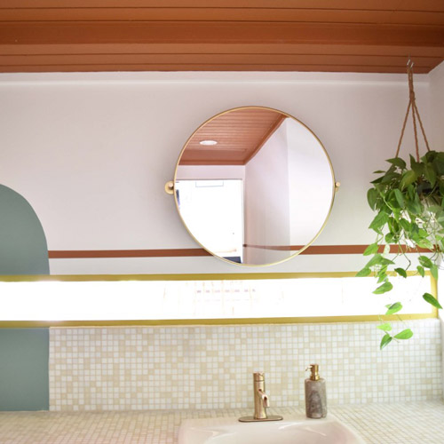 a circular mirror over the sink in a bathroom designed by Brand*Eye Home