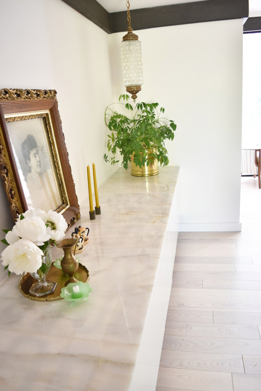 a marble counter with framed photo, flowers, and tall candles along the side of a dining room designed by Brand*Eye Home