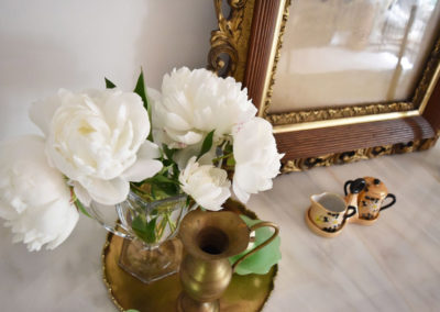 detail of white flowers in a glass vase on a bronze tray next to ceramic saucers on a marble counter