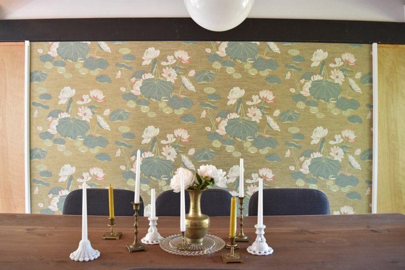 a collection of candles on a wood dining table in front of water lily wallpaper in a dining room designed by Brand*Eye Home