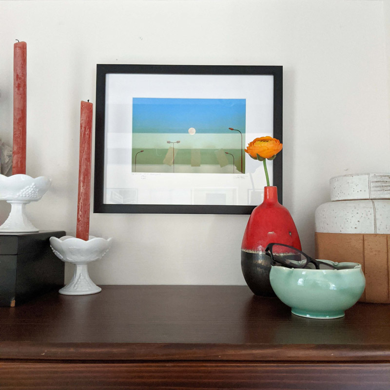 candles, framed artwork, and vases adorn a dresser in a dressing room designed by Brand*Eye Home
