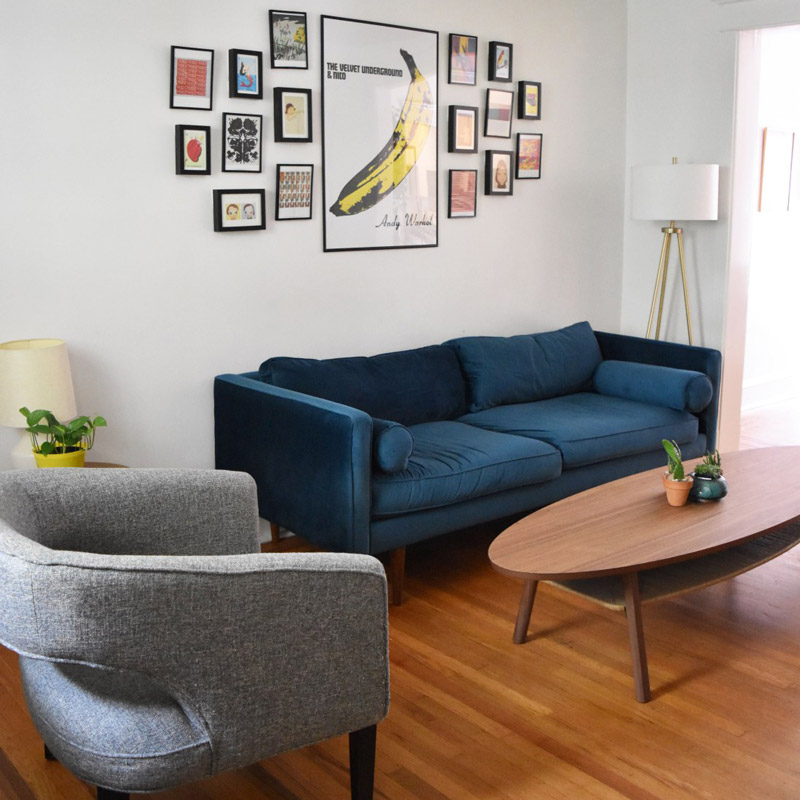 a midcentury modern living room and entrance area with blue sofa, grey chair, and oval coffee table, designed by Brand*Eye Home