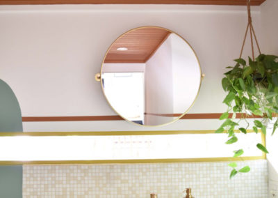 sink in a cream checkered tile countertop with a circular mirror on the wall above and hanging plant in a bathroom designed by Brand*Eye Home