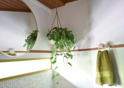 a circular mirror and towel hook on either side of a hanging plant in the corner of a bathroom designed by Brand*Eye Home