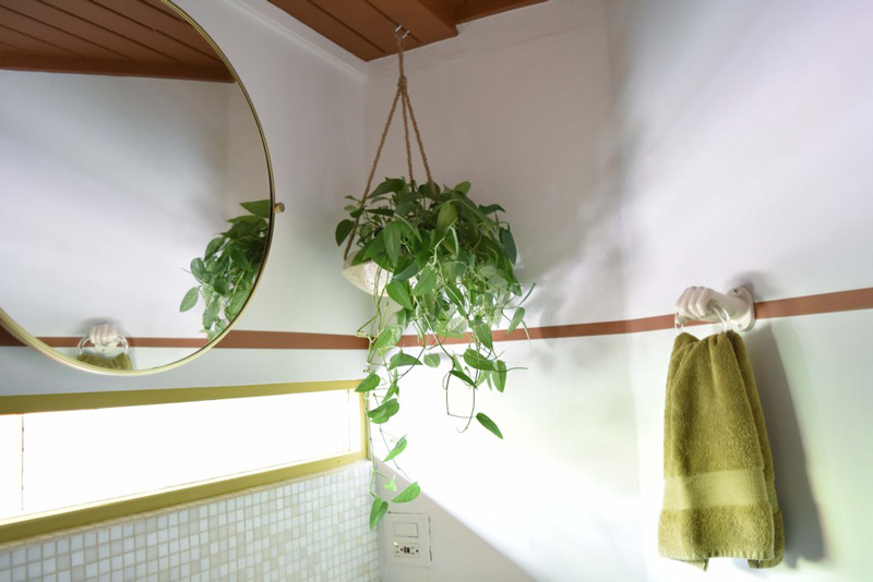 a circular mirror and towel hook on either side of a hanging plant in the corner of a bathroom designed by Brand*Eye Home