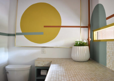 a framed mural of a yellow circle with seafoam and terracotta lines on the wall above a toilet in a bathroom designed by Brand*Eye Home