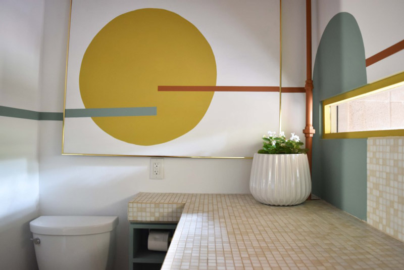 a framed mural of a yellow circle with seafoam and terracotta lines on the wall above a toilet in a bathroom designed by Brand*Eye Home