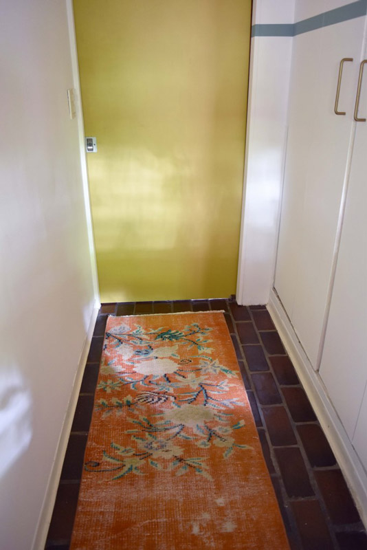 a narrow, floral-patterned rug in the entryway to a bathroom designed by Brand*Eye Home
