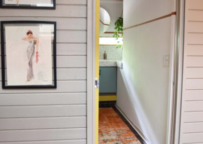 an open doorway to a bathroom designed by Brand*Eye Home, with framed Varga girl prints on the wall