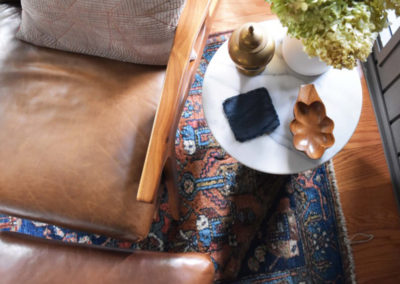 overhead shot of the detail on a small side table with flowers in a vase, carved wood decorations, and coaster in a reading nook designed by Brand*Eye Home