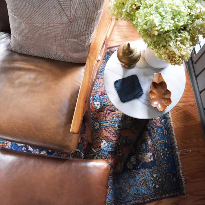 overhead shot of the detail on a small side table with flowers in a vase, carved wood decorations, and coaster in a reading nook designed by Brand*Eye Home