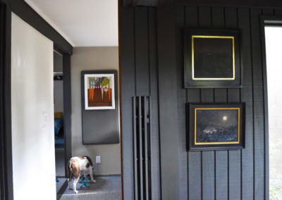 Framed paintings on the wall near a hallway that leads away from the reading nook designed by Brand*Eye Home