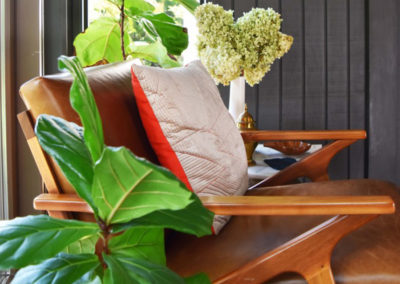 side view of a leather-cushioned midcentury modern chair next to a potted plant in a reading nook designed by Brand*Eye Home