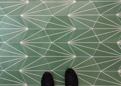 downward look at Brandi's feet standing on green art deco hexagon tile in a bathroom she designed