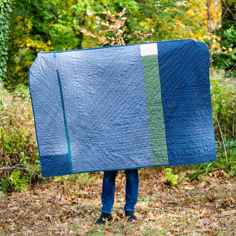 Brandi holding up a blue and green handmade Brand*Eye Home quilt