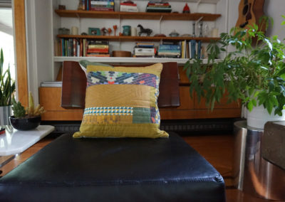 a patterned quilt pillow with a yellow base color handmade by Brand*Eye Home, set on a leather-cushioned chair