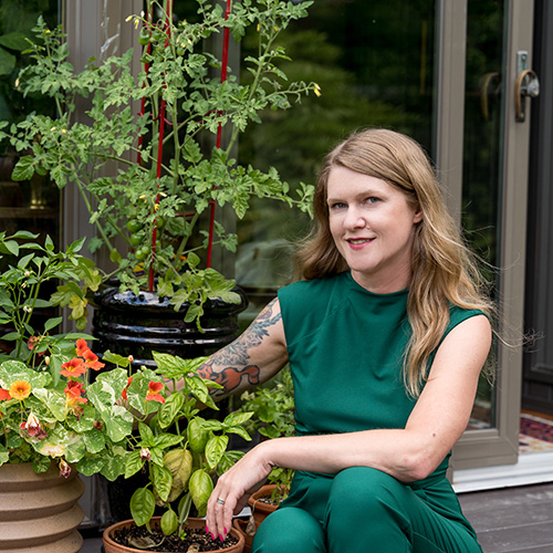 Brandi Adoff of Brand*Eye Home kneeling next to an assortment of potted plants