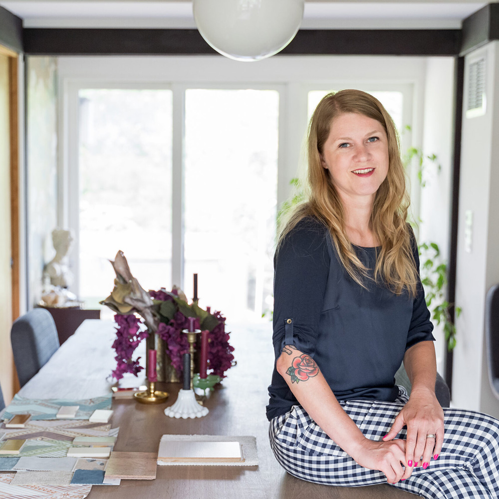 Brandi Adoff of Brand*Eye Design sitting on a dining table with pattern swatches sitting on it