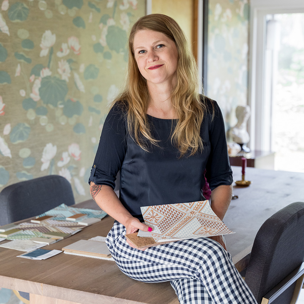 Brandi Adoff of Brand*Eye Design sitting on a dining table with pattern swatches sitting on it